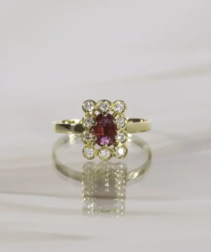 Bague en or jaune au plateau rectangulaire centré d'un rubis taillé en ovale souligné de diamants ronds brillantés posée sur un fond neutre beige