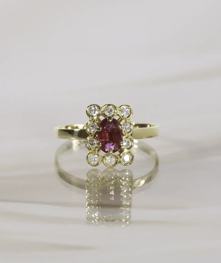 Bague en or jaune au plateau rectangulaire centré d'un rubis taillé en ovale souligné de diamants ronds brillantés posée sur un fond neutre beige