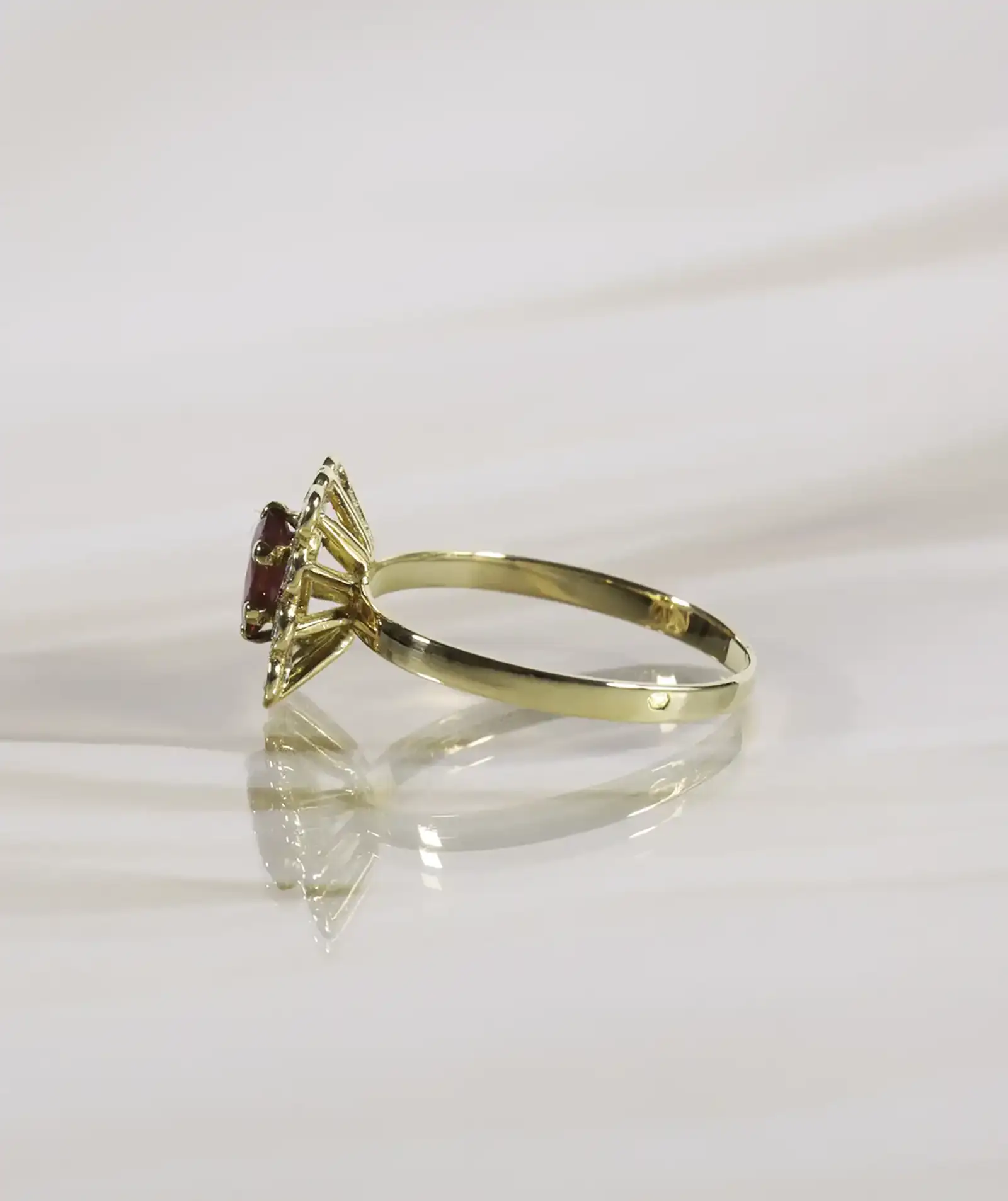 Bague marguerite en or forme rectangulaire serti d'un rubis posée sur le côté, fond neutre beige