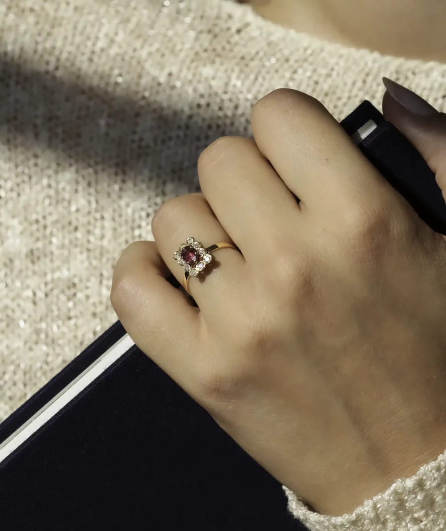 Bague vintage en or rectangulaire surmontée d'un rubis ovale entouré de diamant portée sur une main tenant un livre